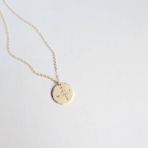 Puede incluir: Collar de oro con un colgante de br&uacute;jula. La br&uacute;jula tiene una estrella en el centro y las letras N, S, E y W alrededor del borde.