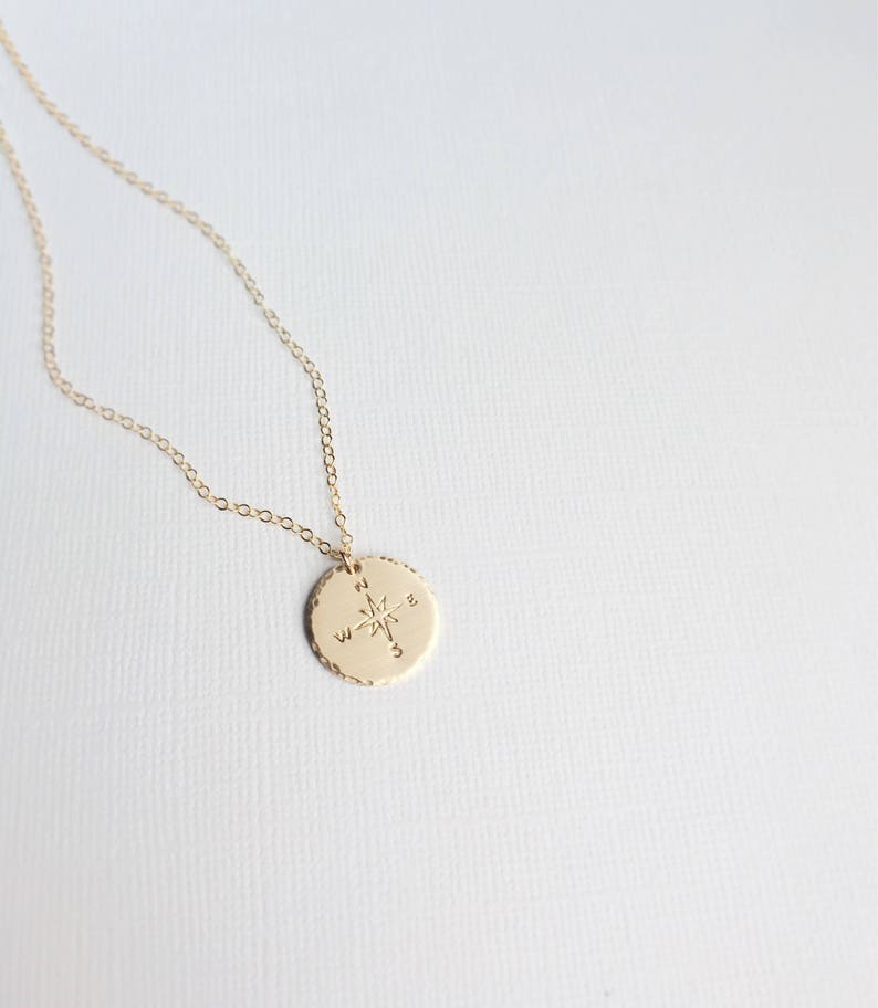 Puede incluir: Collar de oro con un colgante de br&uacute;jula. La br&uacute;jula tiene una estrella en el centro y las letras N, S, E y W alrededor del borde.
