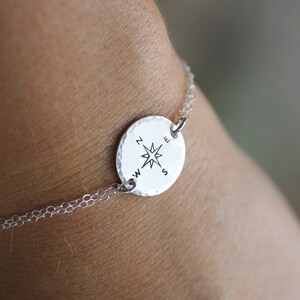 May include: A silver bracelet with a compass charm. The charm features a compass rose with the letters N, E, S, and W around it.