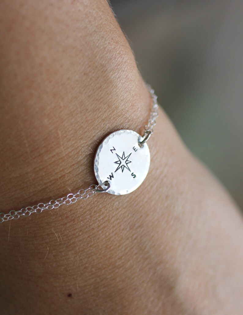 May include: A silver bracelet with a compass charm. The charm features a compass rose with the letters N, E, S, and W around it.