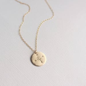Puede incluir: Collar de oro con un colgante de br&uacute;jula en una cadena delicada. La br&uacute;jula tiene una estrella en el centro y las direcciones norte, sur, este y oeste.