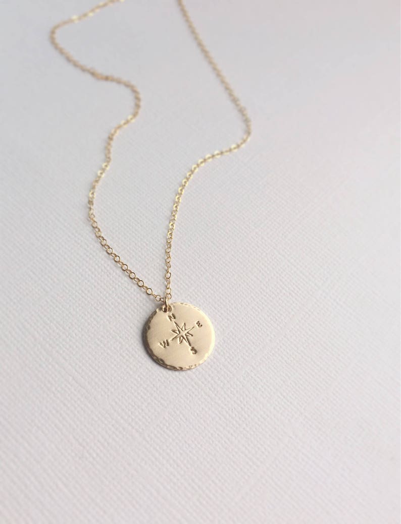 Puede incluir: Collar de oro con un colgante de br&uacute;jula en una cadena delicada. La br&uacute;jula tiene una estrella en el centro y las direcciones norte, sur, este y oeste.