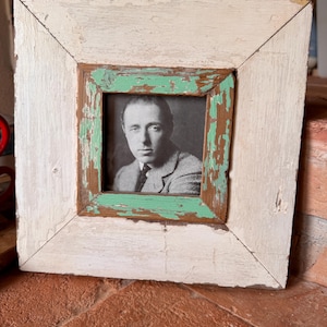 Op de afbeelding: Vierkante, verweerde houten fotolijst met een zwart-wit portret. De lijst heeft een witte buitenrand, een turquoise binnenrand en een bruine houten kern. Het portret toont een man in een pak.