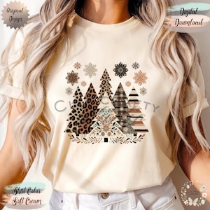 May include: Soft cream-colored t-shirt featuring a festive design of stylized Christmas trees with various patterns, including leopard print and plaid. The design includes snowflakes and the text "Original Design" and "Digital Download".