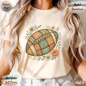 May include: Soft cream-colored t-shirt featuring a patchwork football design surrounded by floral elements. The football has a quilted pattern with various floral and plaid fabrics. The design includes daisies and peach-colored flowers. Text on the shirt reads "Original Design" and "Digital Download".
