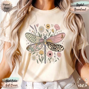 May include: Soft cream-colored t-shirt featuring a dragonfly design with floral and geometric patterns. The dragonfly's wings are adorned with checkered, floral, and leopard print designs. The shirt also has the text "Original Design" and "Digital Download".