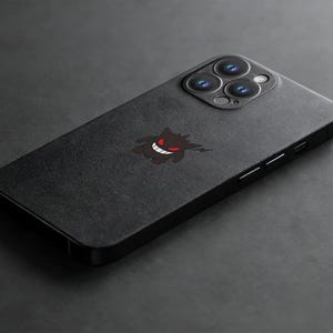 K&ouml;nnte beinhalten: Schwarze Smartphone-H&uuml;lle mit einem Gengar-Motiv. Die H&uuml;lle hat eine matte Oberfl&auml;che und zeigt ein stilisiertes Bild von Gengar mit rotem Mund und Augen. Die Kameralinsen des Telefons sind oben sichtbar.
