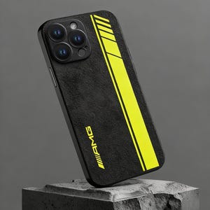 Op de afbeelding: Zwarte telefoonhoes met een getextureerd oppervlak en een neongeel streepontwerp. De hoes heeft het AMG-logo in geel. De telefoonhoes is schuin geplaatst, met de cameralenzen in beeld.