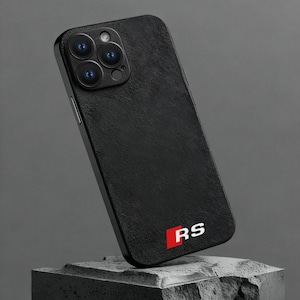 Könnte beinhalten: Schwarze Handyhülle mit strukturierter Oberfläche, mit einem Kameramodul mit mehreren Linsen. Auf der Hülle sind die Buchstaben "RS" in Weiß auf rotem Hintergrund zu sehen. Die Handyhülle wird auf einem dunkelgrauen, strukturierten Block präsentiert.