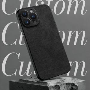 Puede incluir: Funda de teléfono negra con superficie texturizada, con un módulo de cámara con múltiples lentes. La palabra "Custom" se muestra en una fuente estilizada, junto con el texto "Custom car pattern". La funda del teléfono se muestra sobre un bloque de piedra.