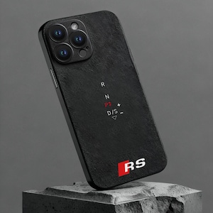 Pode incluir: Capa de telefone preta texturizada com um módulo de câmera e as letras "R", "N", "P", "D/S" e "RS" em vermelho e branco. A capa é exibida em um fundo cinza escuro.