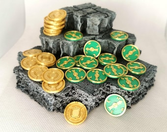 May include: A collection of gold and green compass tokens on a gray rock base. The tokens are arranged in a pile and scattered around the base.