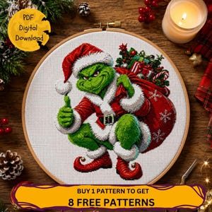 May include: A cross-stitch pattern in a wooden embroidery hoop featuring a green character wearing a red Santa hat, coat, and shoes, holding a large red sack filled with gifts and candy canes, with white snowflakes on the sack and a yellow badge.