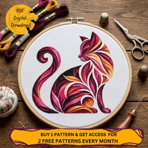 May include: A cross-stitch cat design in a wooden embroidery hoop. The cat is rendered in shades of red, pink, and yellow. The image includes text that says "PDF Digital Download" and "BUY 1 PATTERN & GET ACCESS FOR 2 FREE PATTERNS EVERY MONTH."