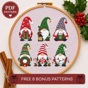 May include: A cross-stitch pattern in a wooden embroidery hoop featuring six gnomes on light pink fabric. The gnomes wear hats in red, green, and grey with holiday motifs like snowflakes, stripes, and hearts, holding items like gifts, lanterns, and candy.