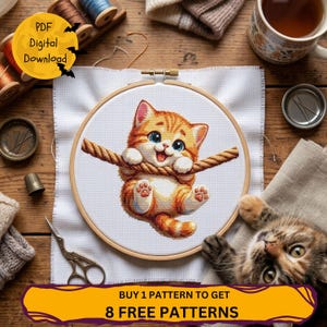 Puede incluir: Un proyecto de punto de cruz en un bastidor de madera que muestra un gatito atigrado naranja colgado de una cuerda. La tela blanca está rodeada de artículos de costura, como carretes de hilo, un dedal, tijeras y una taza de té.