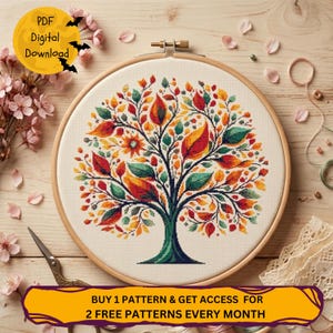 May include: A cross-stitch design of a tree with autumnal-toned leaves, displayed in a wooden embroidery hoop. The leaves are red, orange, and green. The text "PDF Digital Download" is in a yellow circle with bats. The text "BUY 1 PATTERN & GET ACCESS FOR 2 FREE PATTERNS EVERY MONTH" is in a yellow banner.
