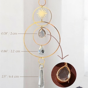 May include: A gold-colored suncatcher with a sunburst design, clear crystal accents, and a total length of 18.9 inches. The suncatcher features a teardrop-shaped crystal pendant and a circular design. The text "SUN AURA" is visible.