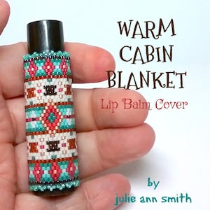 May include: A beaded lip balm cover with a geometric pattern in shades of red, white, brown, and turquoise. The cover is labelled "Warm Cabin Blanket Lip Balm Cover" and "by julie ann smith".