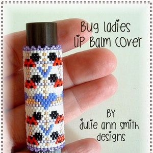 May include: A beaded lip balm cover with a bug design. The cover is white with red, black, blue, and gold beads. The text "Bug ladies lip balm cover" is above the cover and "BY julie ann smith designs" is below the cover.
