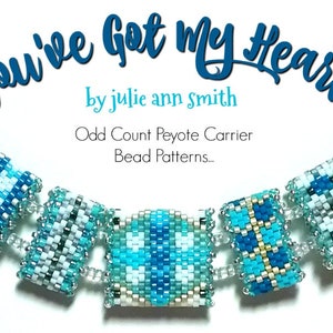 Op de afbeelding: Een kralenarmband met een blauw, wit en gouden kleurenschema. De armband is gemaakt van vierkante kralen en heeft een patroon van strepen en vierkanten. De armband heeft de titel "You've Got My Heart" van Julie Ann Smith. De tekst "Odd Count Peyote Carrier Bead Patterns..." is ook inbegrepen.