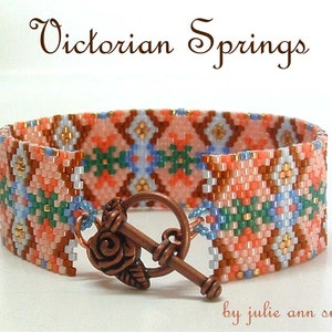 May include: A beaded bracelet with a geometric pattern in shades of peach, brown, green, and blue. The bracelet has a copper clasp with a rose design. The text "Victorian Springs by julie ann smith" is visible below the bracelet.