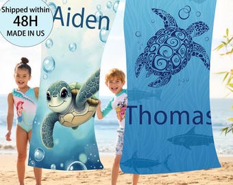 May include: Two beach towels hanging on a clothesline. One towel features a cartoon sea turtle and the name "Aiden". The other towel has a blue sea turtle design and the name "Thomas". Both towels are blue and white.