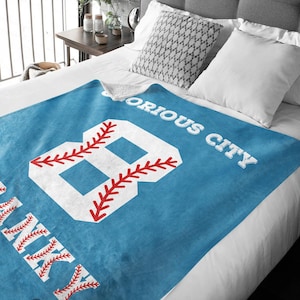 May include: A blue fleece blanket with a white baseball number 8 and the text "Glorius City" in white. The baseball number has red stitching.