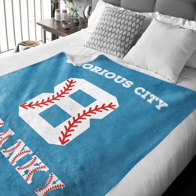 May include: A blue fleece blanket with a white baseball number 8 and the text "Glorius City" in white. The baseball number has red stitching.