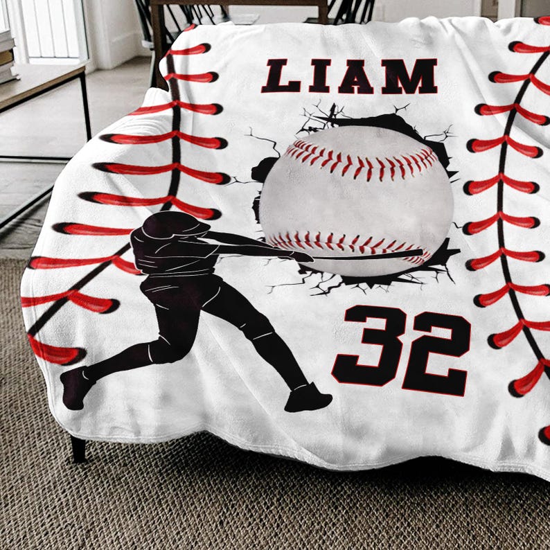 May include: White baseball themed fleece blanket with red stitching, a baseball breaking through the stitching, a baseball player silhouette, the name "LIAM" and the number "32" in black.