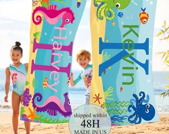 May include: Two personalized beach towels with sea creature designs, including seahorses and octopuses, are displayed on a clothesline. The towels feature the names "Harvey" and "Kevin" in large letters. The towels are decorated with an underwater theme.
