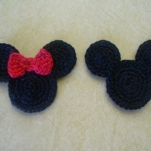 May include: Two crocheted mouse head shapes, one with a red bow. The mouse heads are black and the bow is red.