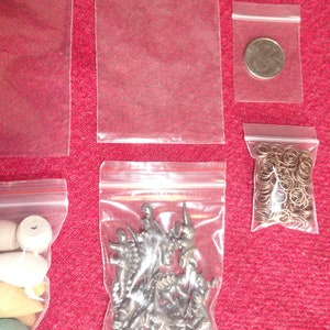 May include: Five clear plastic bags with zipper closures. The bags contain various items, including small metal figurines, a coin, and a chain of small metal rings.