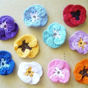 May include: Ten crocheted flower embellishments in various colors, including purple, blue, yellow, white, pink, orange, and red. Each flower has a center with a different color.