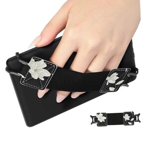 May include: Black e-reader case with a white floral design strap. The strap has two adjustable buckles. The case is held in a hand.