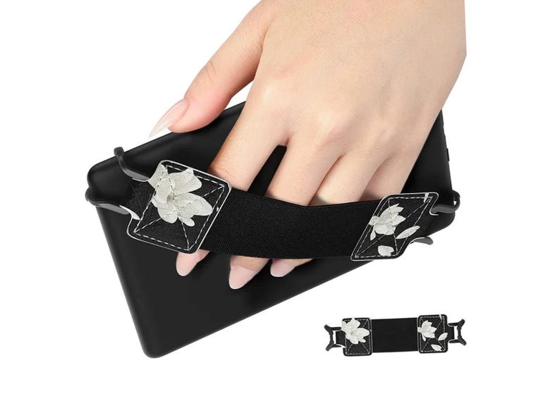 May include: Black e-reader case with a white floral design strap. The strap has two adjustable buckles. The case is held in a hand.