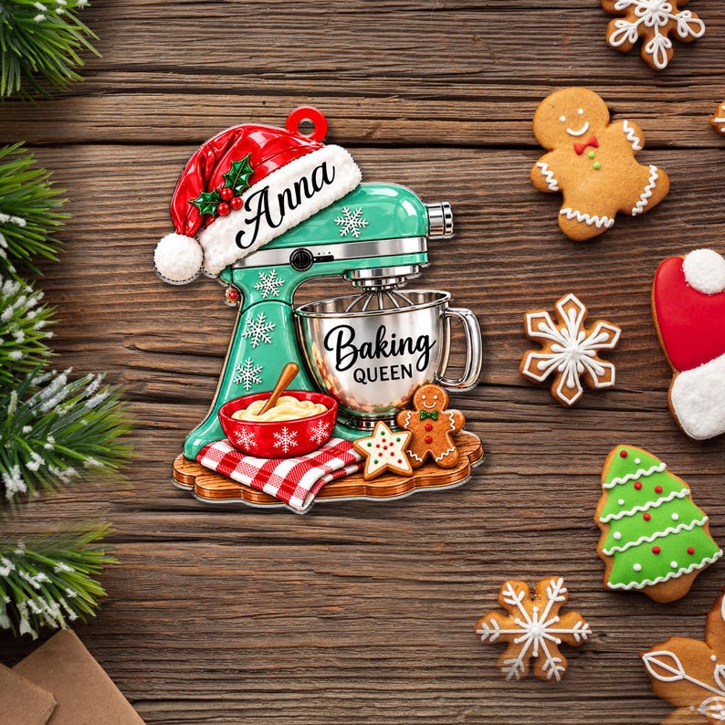 May include: A teal stand mixer ornament featuring a red Santa hat with the name Anna, a silver mixing bowl labeled Baking Queen, a red bowl with dough, a red and white checkered towel, and a small gingerbread man and star cookie.