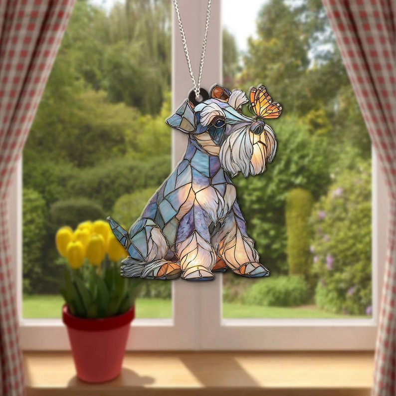 May include: A decorative hanging ornament featuring a Schnauzer dog design with a butterfly. The dog is rendered in a stained-glass style, with blue, purple, and orange hues. It hangs from a silver chain, perfect for a window or rearview mirror.