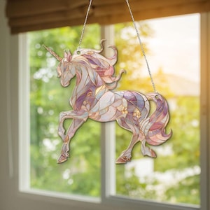 以下が含まれることがあります： ステンドグラス風ユニコーンサンキャッチャー。紫、ピンク、ゴールドの色合いで描かれたユニコーンは、なびくたてがみと尾が特徴です。銀色のチェーンで吊り下げられており、窓や壁の装飾に最適です。
