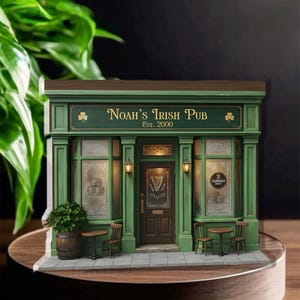 Könnte beinhalten: Ein detailliertes Miniaturmodell von Noah's Irish Pub, bemalt in Grün und Braun. Das Pub hat ein Schild mit der Aufschrift "Noah's Irish Pub Est. 2000". Kleine Tische und Stühle sind draußen aufgestellt, mit einem Fass und einem kleinen Baum.