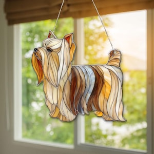 Könnte beinhalten: Glasfenster-Suncatcher eines Yorkshire Terrier-Hundes. Der Hund ist in Braun-, Beige- und Cremetönen mit detailliertem Design dargestellt. Er hängt an einer silbernen Kette, ideal für eine Fenster- oder Wanddekoration. Ein dekorativer Artikel.