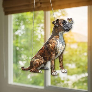 Könnte beinhalten: Dekorativer Hängeornament mit einem Boxerhund und einem Schmetterling auf der Nase. Der Hund hat ein gestromtes Fell mit weißen Akzenten, und der Schmetterling hat gelbe und schwarze Markierungen. Das Ornament hängt an einer silbernen Kette.