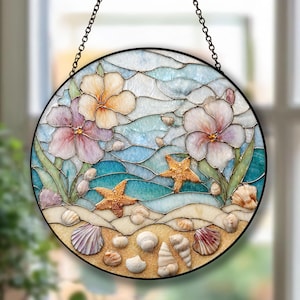 Könnte beinhalten: Runde Glasfensterkunst mit einer Strandszene mit Blumen, Seesternen und Muscheln. Das Kunstwerk hat einen schwarzen Metallrahmen und wird von einer Kette gehalten. Die Farben umfassen Blau-, Beige-, Rosa- und Goldtöne.