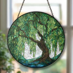 May include: Round stained glass window featuring a weeping willow tree. The tree has a brown trunk and branches with green leaves. The background is a mix of green and white, and the window is framed in black and suspended by a chain.
