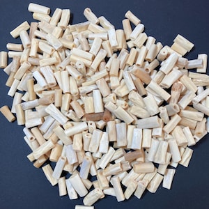 May include: A large collection of small, cylindrical, off-white and beige tube-shaped beads. Each bead features a hollow center and a natural, slightly irregular, textured surface with varying shades of cream, tan, and light brown throughout.