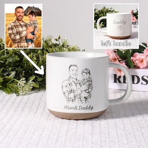 Könnte beinhalten: Weißer Keramikbecher mit braunem Boden und gebogenem Henkel. Der Becher zeigt eine Schwarz-Weiß-Skizze eines Mannes, der ein Kind hält, mit dem Text "Alan & Daddy" darunter. Ein kleineres Bild zeigt den Becher mit dem Text "Daddy" und einem Herzen.