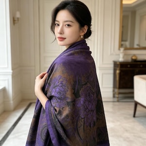 Puede incluir: Una bufanda rectangular con un color base morado intenso y grandes patrones florales detallados en tonos violeta y marrón oscuro. La tela tiene una textura suave y lisa, drapeada sobre los hombros, mostrando un diseño de borde oscuro.
