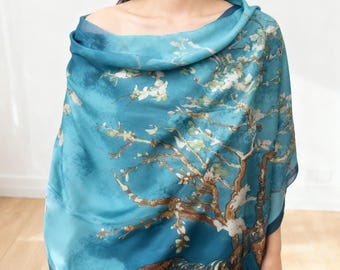 Könnte beinhalten: Türkisfarbener Schal mit einem Aufdruck eines Baumes mit weißen Blüten auf blauem Hintergrund. Der Schal ist über den Schultern drapiert und zeigt die Details und die Farbpalette des Kunstwerks. Das Design erinnert an Kunst und Natur.
