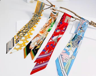 May include: Four colorful silk scarves with various patterns, including floral, feather, and Parisian-themed designs. The scarves are displayed on a branch against a white background. Each scarf has a unique color scheme, such as yellow, orange, red, and blue.