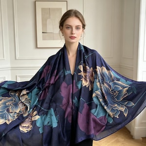 Puede incluir: Una bufanda azul marino con un gran estampado floral en tonos turquesa, morado y beige. La bufanda está drapeada, mostrando el intrincado diseño y la tela fluida. Un accesorio de moda.